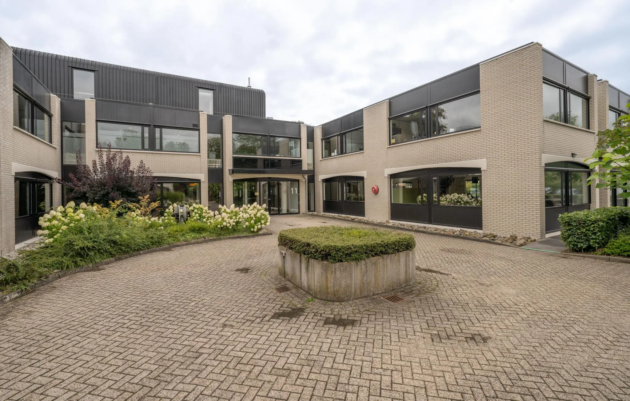 Moderne kantoorvilla aan de Burgemeester Verderlaan met beige bakstenen gevel, zwarte kozijnen en een groene binnentuin.